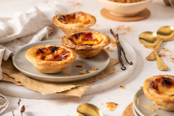 istock Several Pastel de Nata are arranged on plates with cinnamon, vanilla beans, and small golden spoons. 2196619776