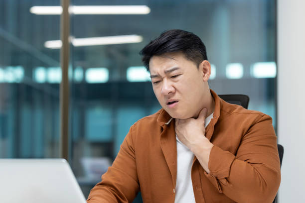 istock Asian man feeling sore throat pain while working on his computer 2196621460