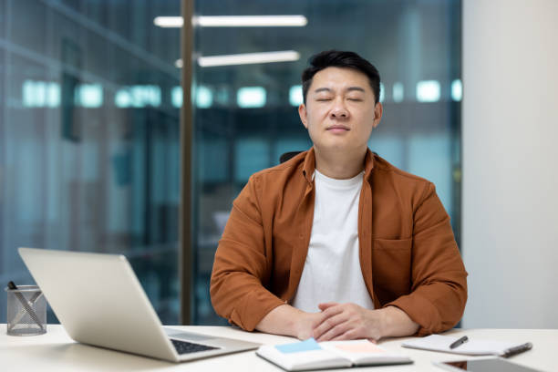 istock Asian businessman meditating at office desk during a work break 2196621461