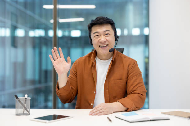 istock Asian man waving cheerfully while wearing a headset in a business environment 2196622276