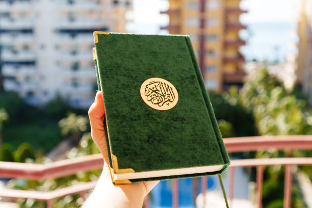 Green Quran Held Outdoors with Sunny Urban Background and Natural Scenery