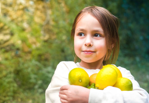 Close up shot of curious little girl smiling as she is watching her mother drip honey into a big glass jug with lemonade. She is watching the honey dissolve in the liquid.