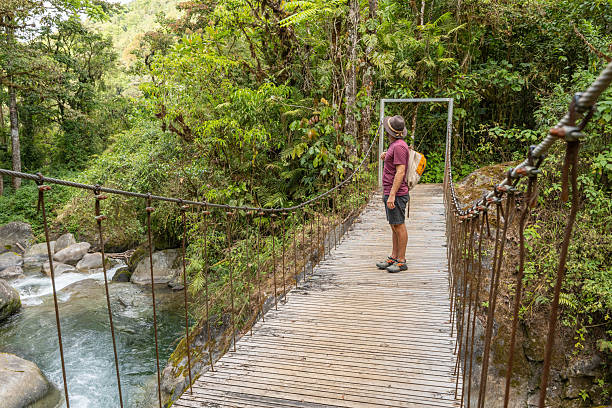 istock Man Walking on Jungle Suspension Bridge with Backpack 2196629672