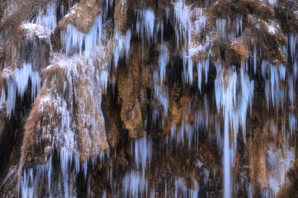 Winter frozen waterfall with icicles on moss-covered rocks in cold evening. Plitvice Lakes, Croatia. Colorful scene with frozen water. Nature background with blue icicles on the rock. Close up