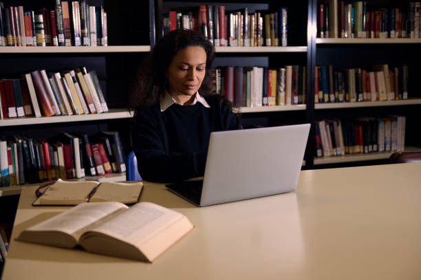 istock Woman studying in a library with a laptop and open books 2196634675