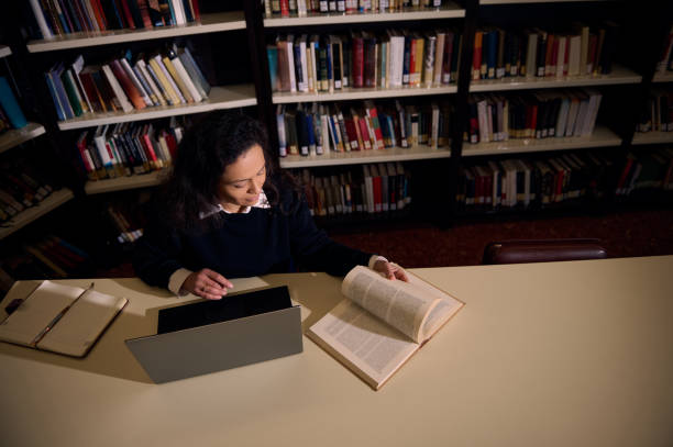 istock Woman studying in a library surrounded by books and using digital resources 2196634682