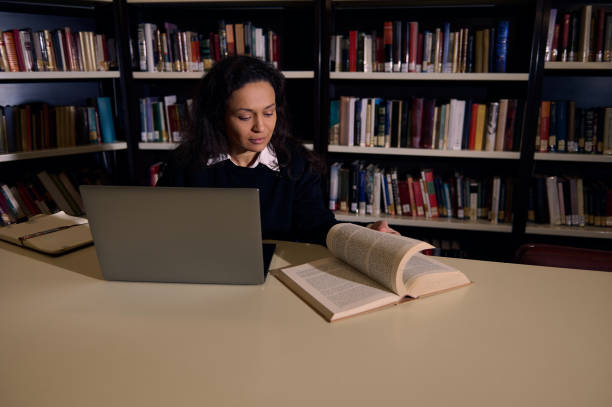 istock Woman Studying in a Library with a Laptop and Open Book 2196634684
