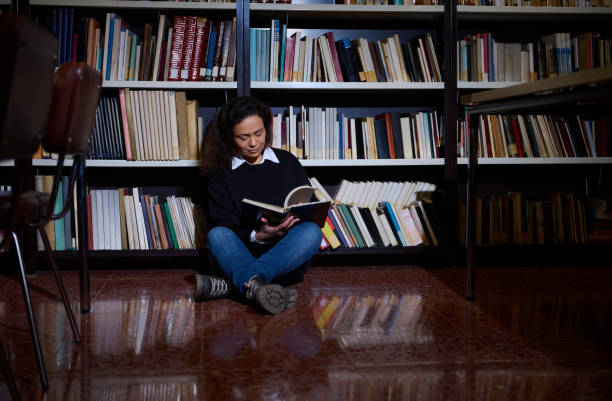 istock Woman reading a book while sitting on the floor in a library 2196634696