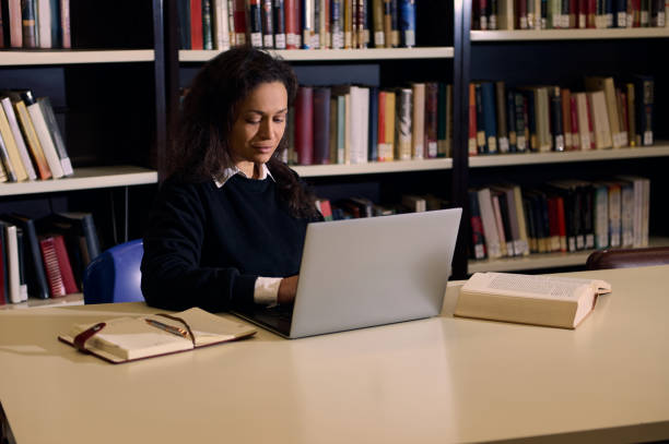 istock Woman studying in library using laptop with open books on the table 2196634697