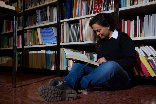istock Woman reading a book while seated in a library aisle 2196634709