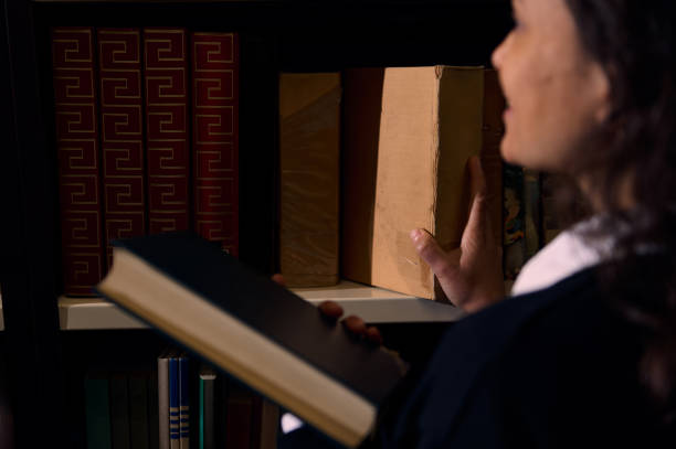 A young student browses a library shelf, selecting a hardcover book while holding another.