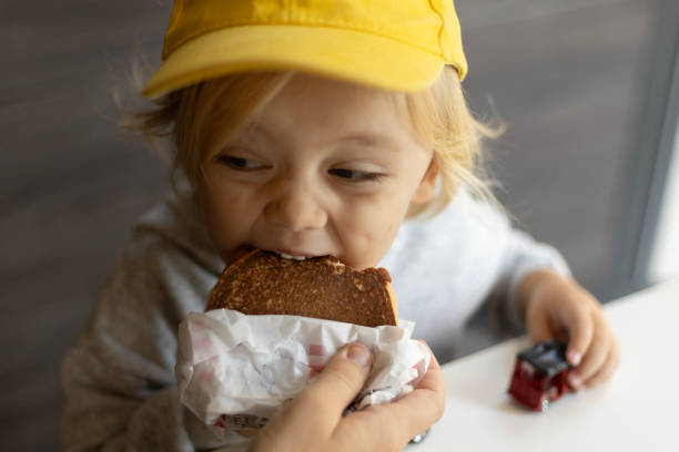 istock a 3-year-old boy wearing a yellow cap is eating a burger 2196636745