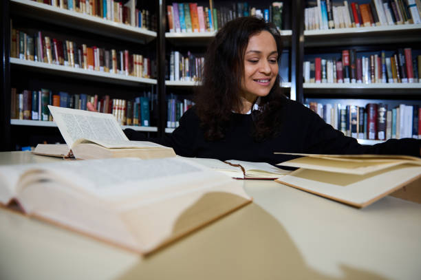 istock Smiling woman studying in a library surrounded by open books on a table 2196637314
