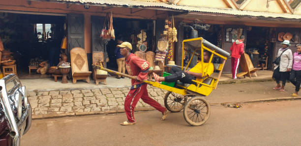 Andasibe, Madagascar - April 29, 2024: One men running with a rickshaw with a local passenger along small shops.