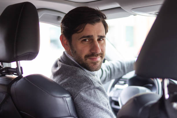istock Young businessman driving a car and looking back at the camera 2196643987