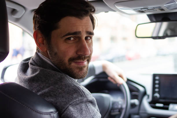 istock Young businessman driving car and looking back at camera 2196644656