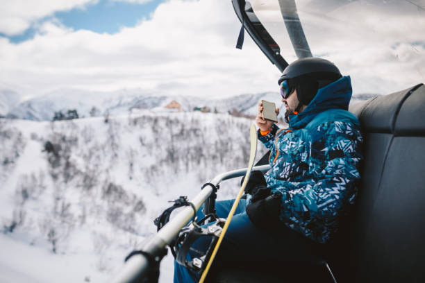 istock Man with Snowboard sitting on a Ski lift, using a smart phone. 2196653715