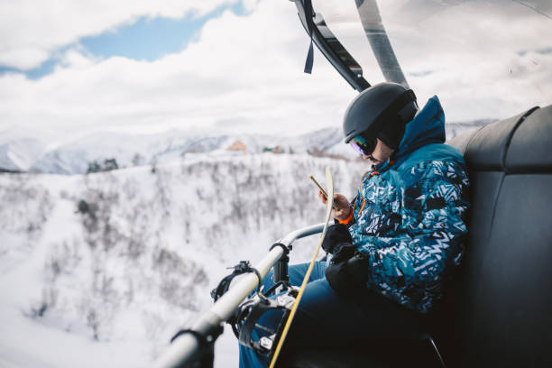 istock Man with Snowboard sitting on a Ski lift, using a smart phone. 2196653725