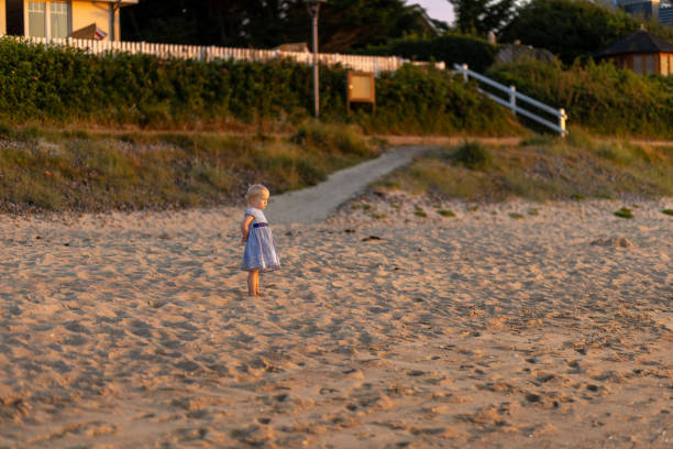 Child explores sandy beach during sunset near a coastal pathway lined with greenery