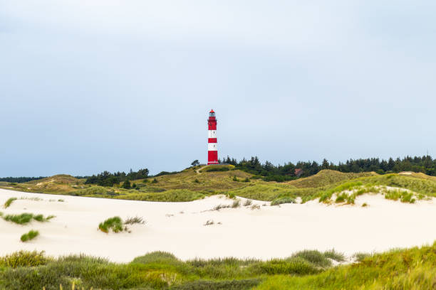 istock Red and white lighthouse standing tall in the sandy dunes under an overcast sky at the coastline 2196657706