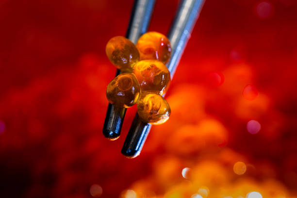 A close-up shot of glowing red caviar delicately held by stainless steel chopsticks, set against a blurry background of vibrant salmon eggs