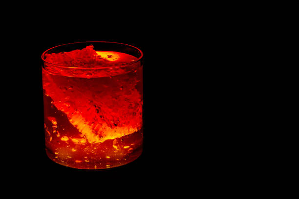 Honeycomb submerged in golden honey inside a crystal-clear cylindrical jar, glowing with vibrant shades of orange, yellow, and red against a black backdrop.
