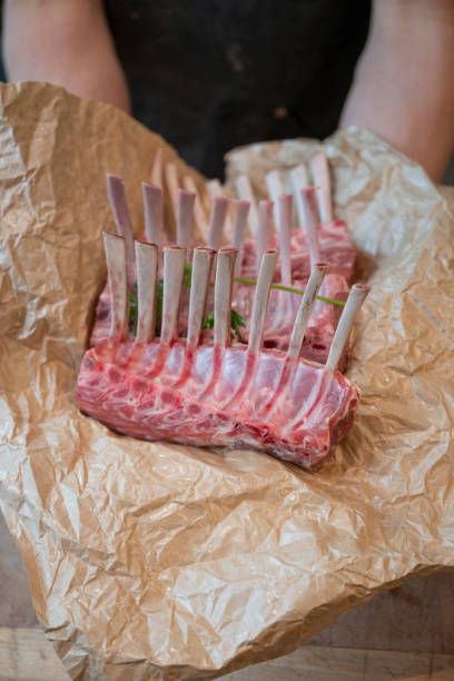 Butcher holds rack of lamb on paper in gourmet butcher shop, Vancouver, B.C.