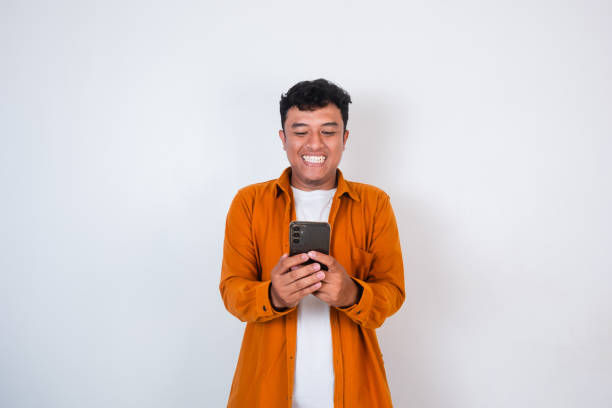 istock Smiling young Asian man in casual shirt using smartphone, chatting online, texting message, looking at smartphone isolated on white background 2196680343
