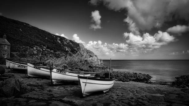 Black and white image of fishing boats on a rocky shore under a dramatic sky, capturing a serene coastal scene.