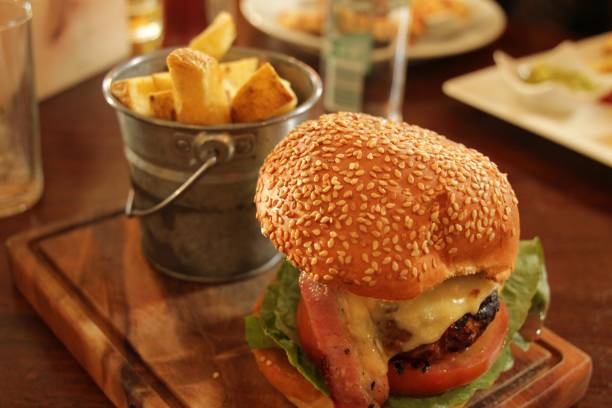 Close-up of a cheeseburger with bacon and fries in a rustic bucket on a wooden board