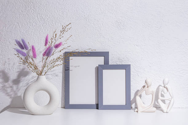 istock decorative objects on a white table in the interior of a modern space. A photo frame, lilac dried flowers in stylish vase, statuette. Front view. 2196686557