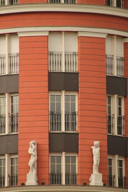 Bilbao, Spain – July 20, 2012: Close-up of an ornate red building facade with white statues and black railings, showcasing architectural details.