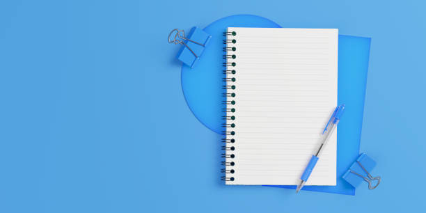 Open spiral notepad with blue pen and paper clips on blue background