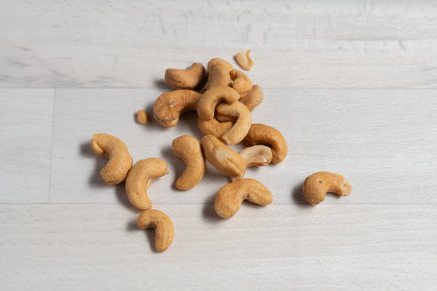 A close-up view of roasted cashews scattered across a light wooden background. This simple, neutral-toned shot highlights the warm, golden colour and curved shape of the nuts, ideal for illustrating healthy snacks, plant-based proteins, or natural food concepts