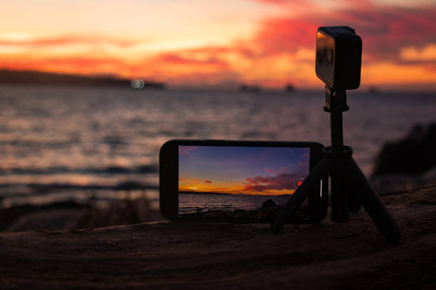 istock Mobile phone and action camera setup capturing ocean sunset on Vancouver beach, with dramatic orange and red sky reflected in phone screen 2196693647
