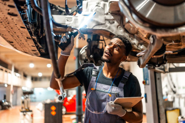 istock Mechanic inspecting car chassis with flashlight and tablet in workshop 2196695175