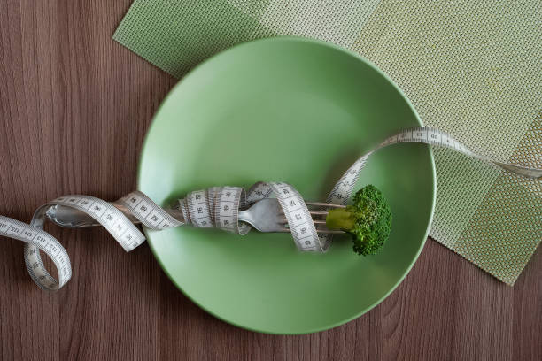 istock Green plate with broccoli on a fork and a white measuring tape on a table background. Diet concept. Healthy eating, lifestyle. 2196696786