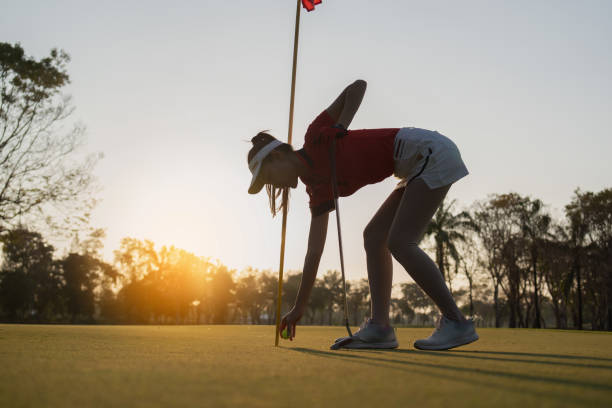 female golfer is putting the ball into the hole.