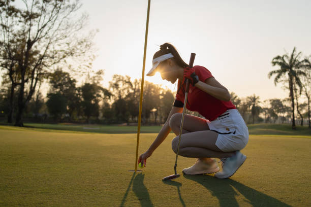female golfer is putting the ball into the hole.