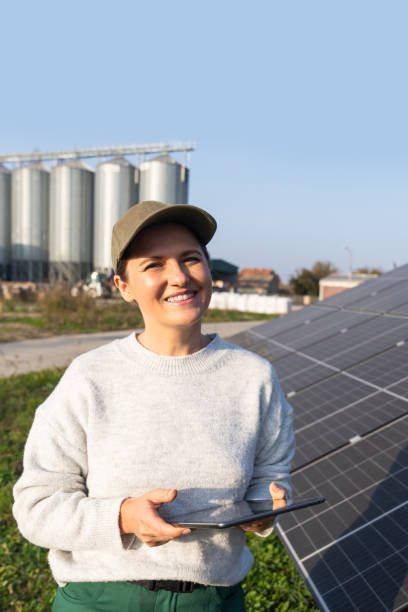 istock Female farmer with digital tablet on a modern farm using solar panels. Agricultural silos in the background. 2196704075