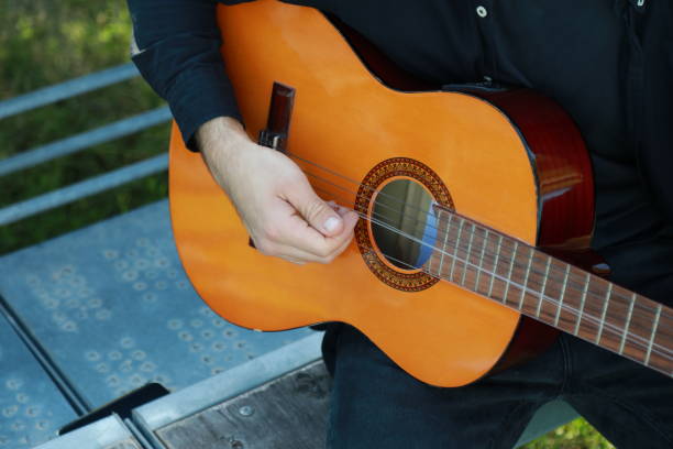 istock Man Tunes Guitar With Tuning Fork Outside 2196705780