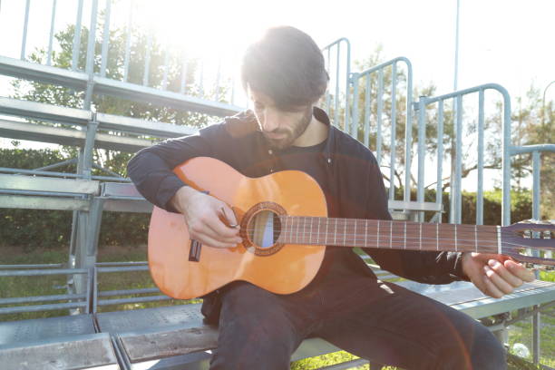 istock Man Tunes Guitar With Tuning Fork Outside 2196705782