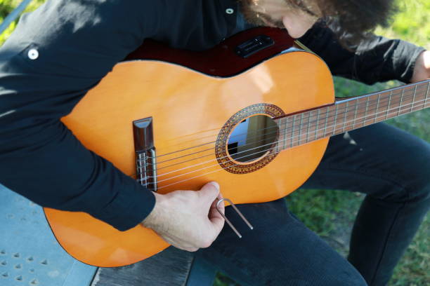 istock Man Tunes Guitar With Tuning Fork Outside 2196705789