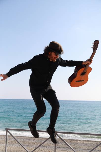 istock Guitar Musician Balancing On Railing Walks At Beach Near Ocean 2196706475