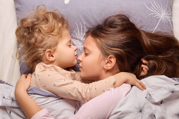 istock Two sisters share a tender moment while sleeping beside each other in a cozy bed during a peaceful afternoon. Their expressions reflect tranquility and love 2196713469