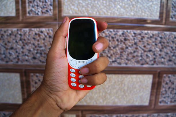 Man holding a keypad mobile phone isolated on texture background. Mini Cell phone buttons and black display and keys dialing in hands. Old 2g, 3g device