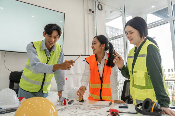 istock Joyful construction team engaging in brainstorming session with project plans and safety gear in a modern office 2196717079