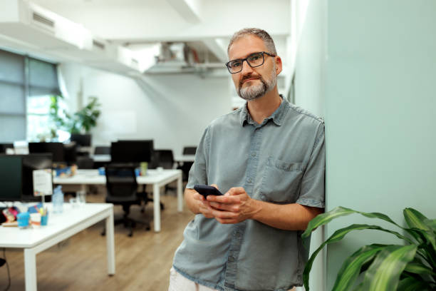 istock Mature businessman posing for camera while using smart phone at the modern office 2196722655