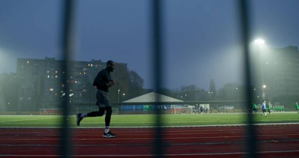 A man in sports clothes runs around the stadium on a cold evening, side view