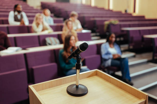 istock Microphone stands on podium, students listening to lecture in university classroom 2196731142
